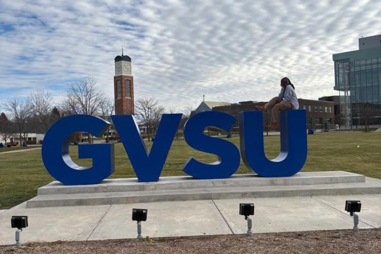 Rebecca sitting on the GVSU signage